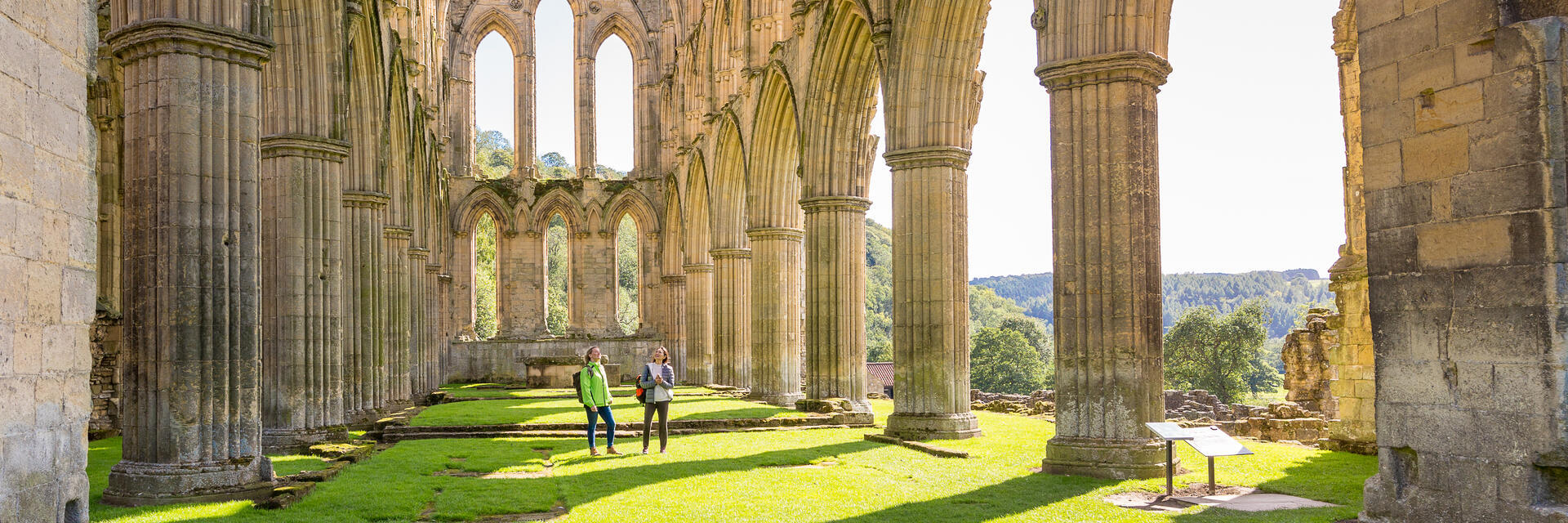 Two female friends in the central nave of a ruined abbey in the sunshine