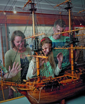 Family with children looking at ancient ship model on display in a museum