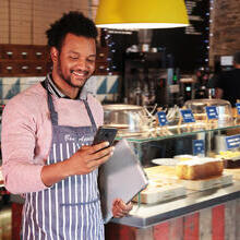 Male cafe owner smiling at his phone in front of the counter in the restaurant