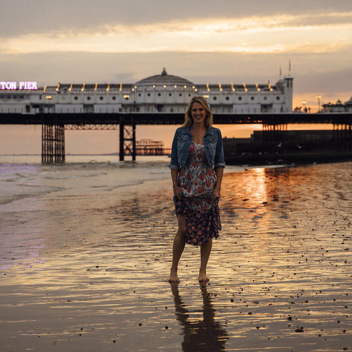 Donna in piedi sulla spiaggia vicino al molo al tramonto