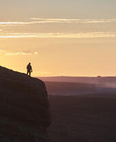 Silhouette of person hiking on large hill at sunset
