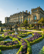 A formal garden with statues and low hedges in front of a stately house