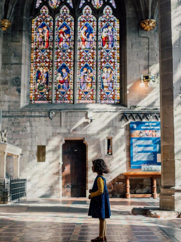 A girl standing in front of a stained glass window in a cathedral