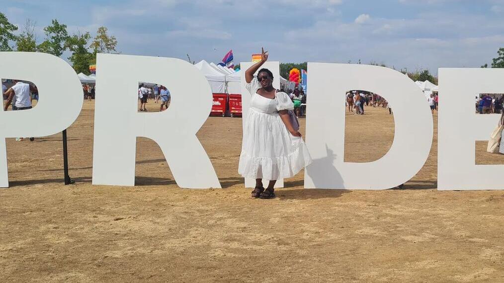 Mujer con vestido blanco delante del cartel del UK Black Pride