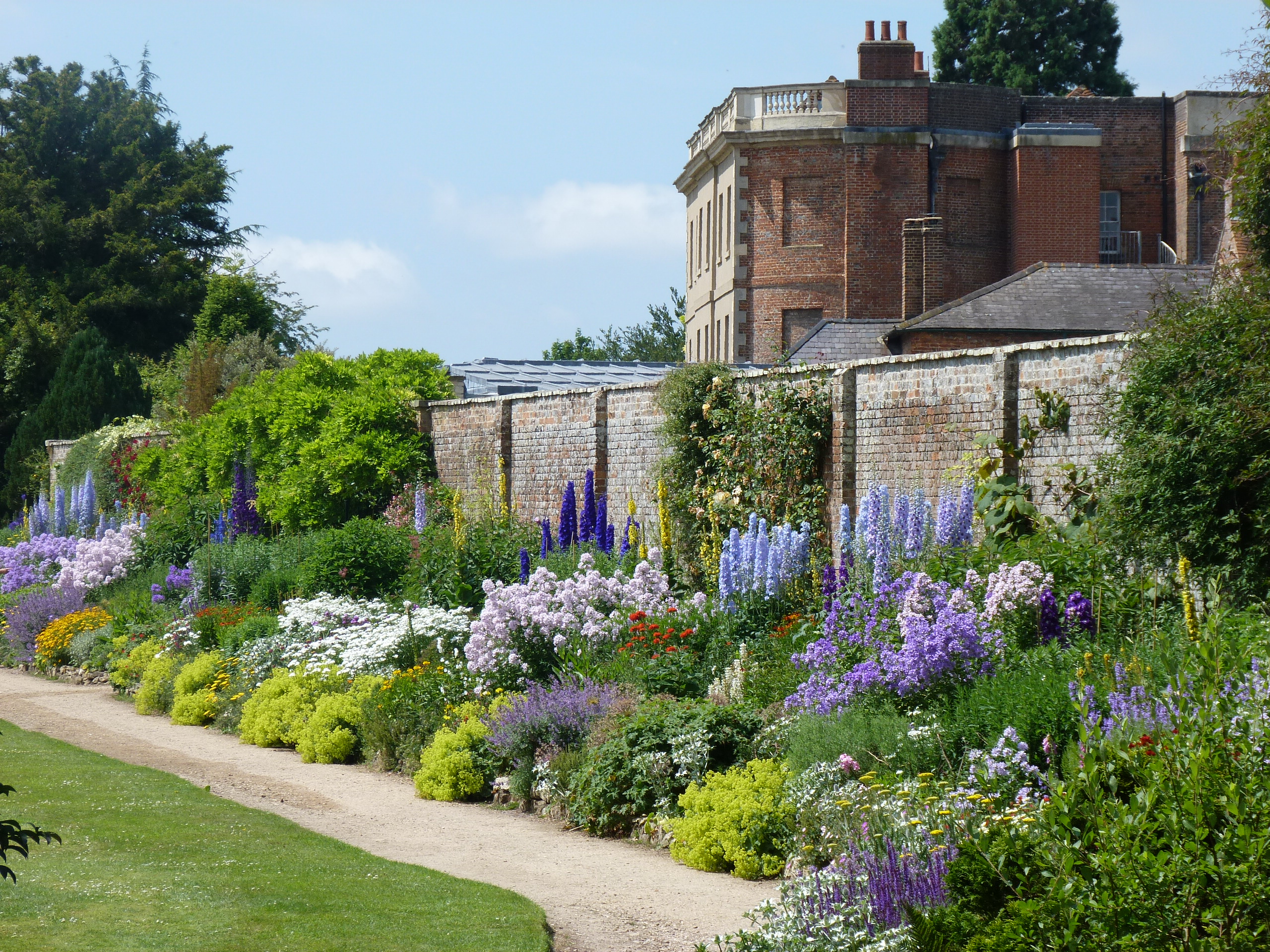 A walkway through a pretty walled garden blooming with flowers.