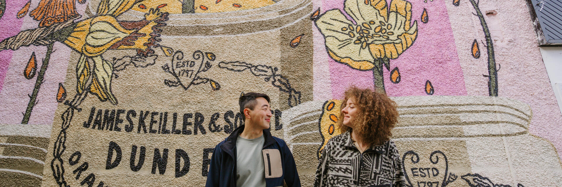 A man and a woman holding hands in front of the marmalade mural.