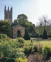 Blumenbeet vor einem georgianischen Bogen und dem Gebäude des Oxford Botanic Garden mit Kirchturm im Hintergrund vor blauem Himmel