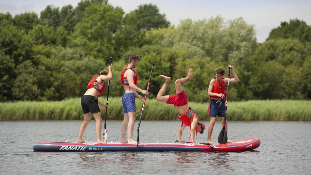 Four men in red life vests standing on a paddleboard