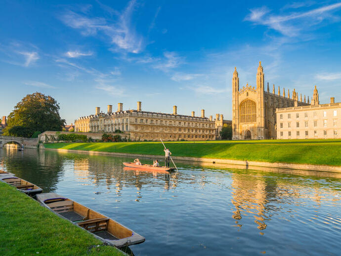 People punting along a river next to a college and chapel.