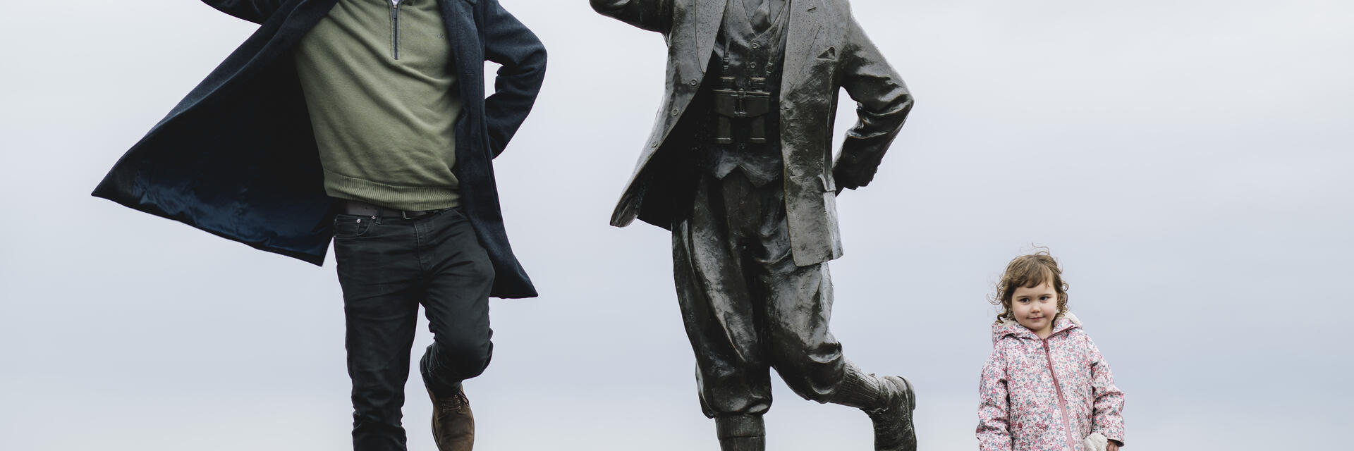 View of man, female child and statue of a man in front of the sea
