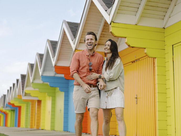 A man and woman laughing outside colourful beach huts