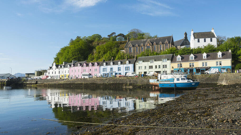 Des maisons aux couleurs pastel bordent le port de pierre de Portree par une journée ensoleillée.