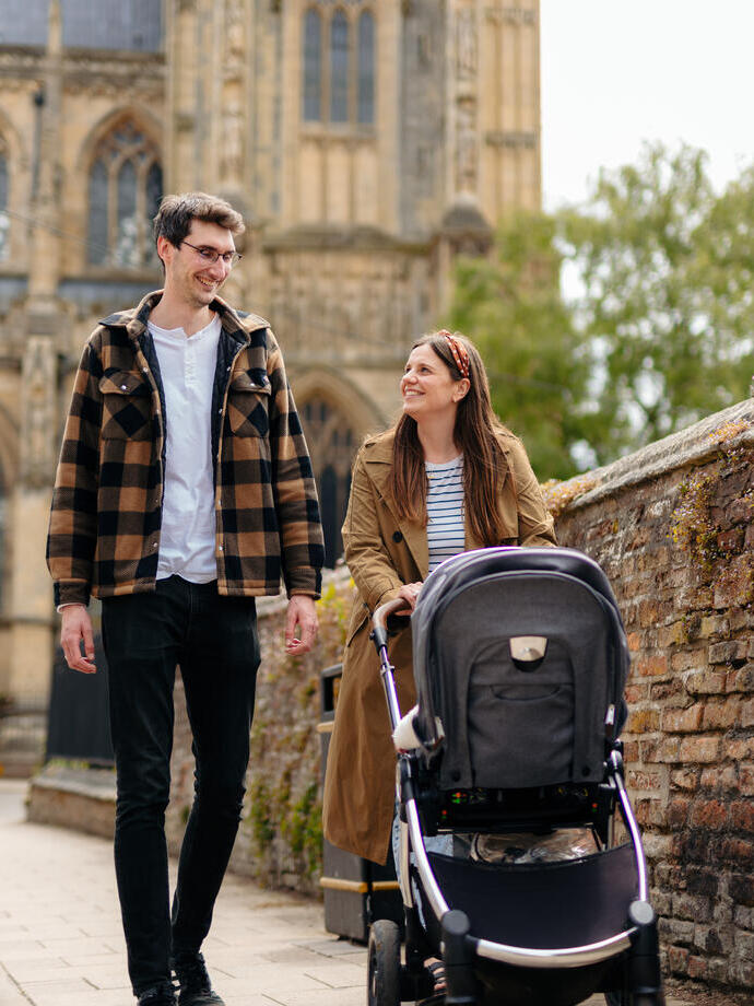 A man and a woman walk with a pushchair in front of a heritage building