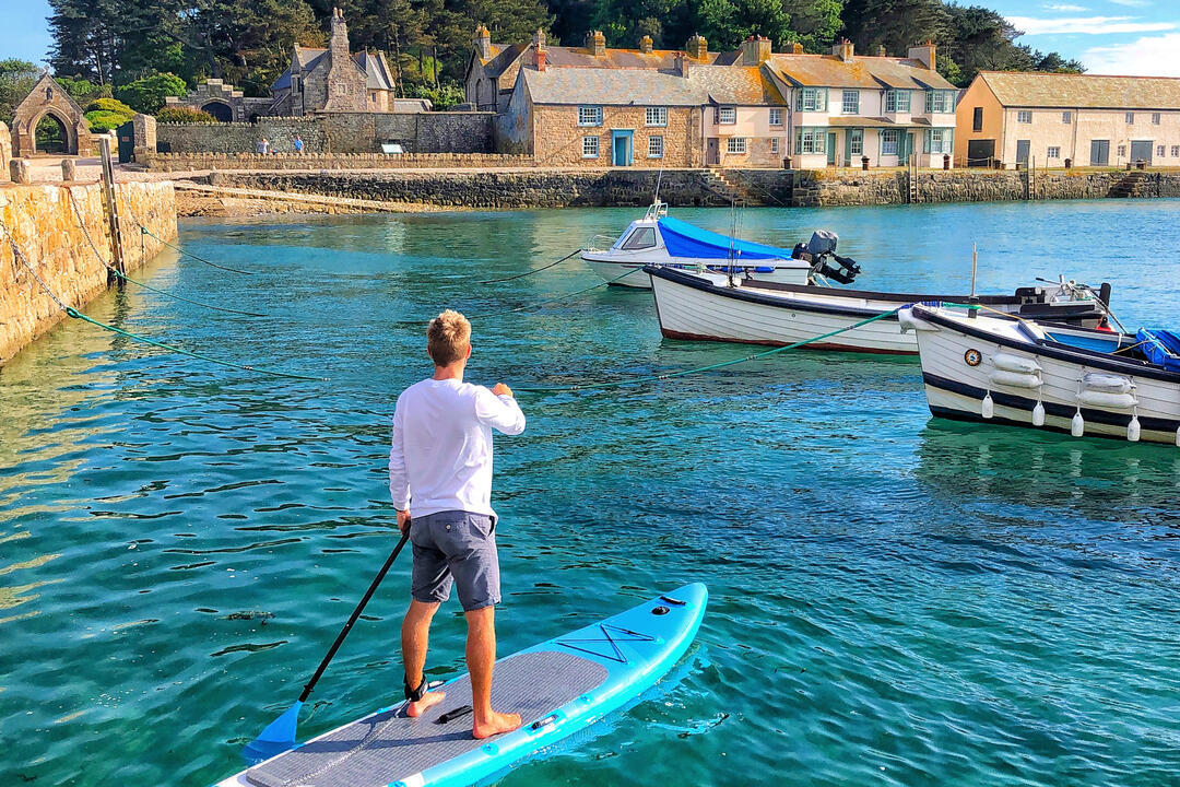A man paddle-boarding in a harbour towards a church on top of a hill