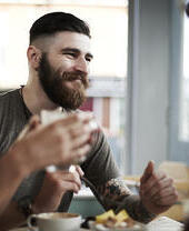 Young bearded male with tattoos socializing with group of friends in cafe.