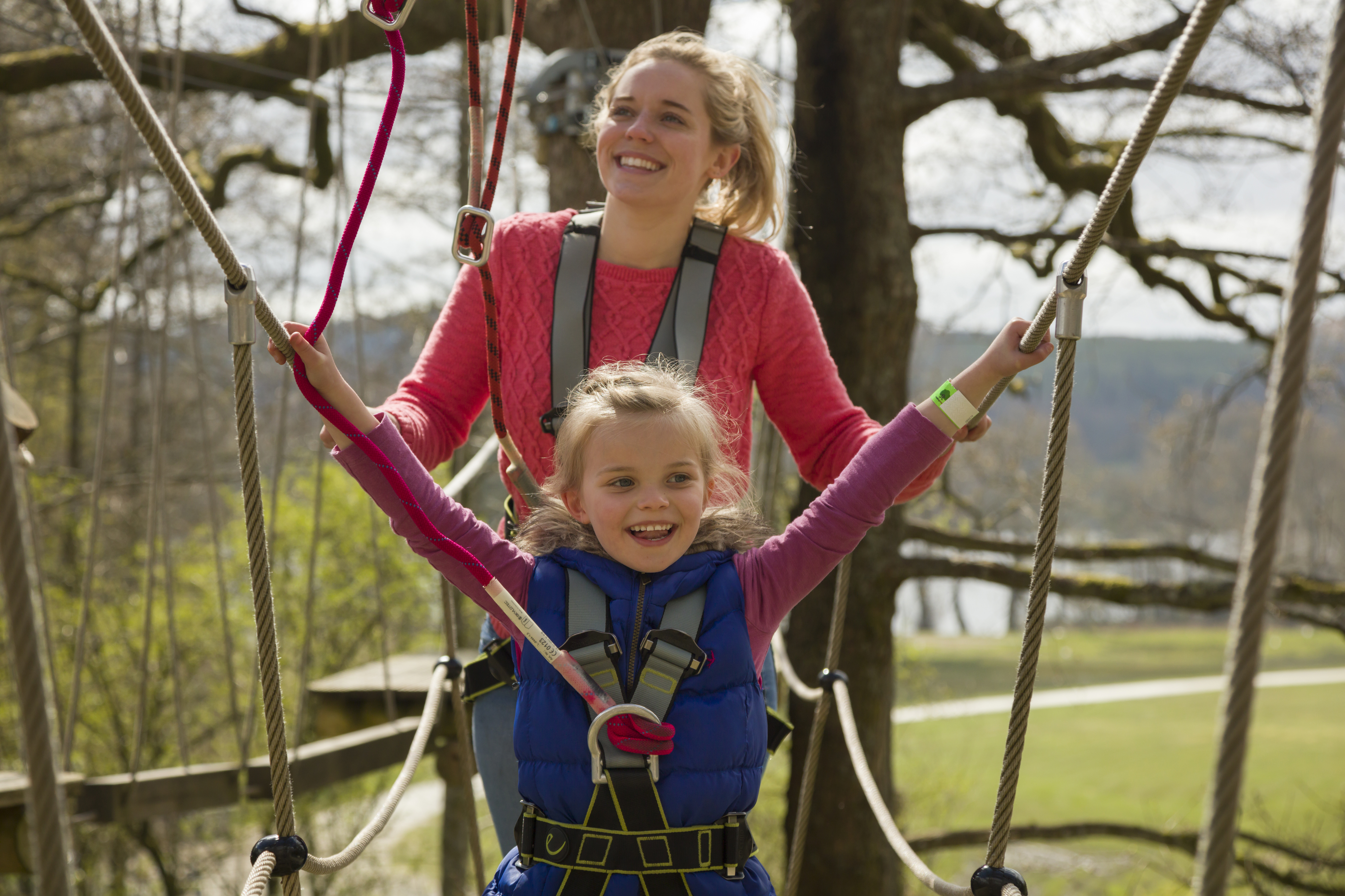 Woman and child wearing safety harnesses, on a rope bridge at a tree top experience