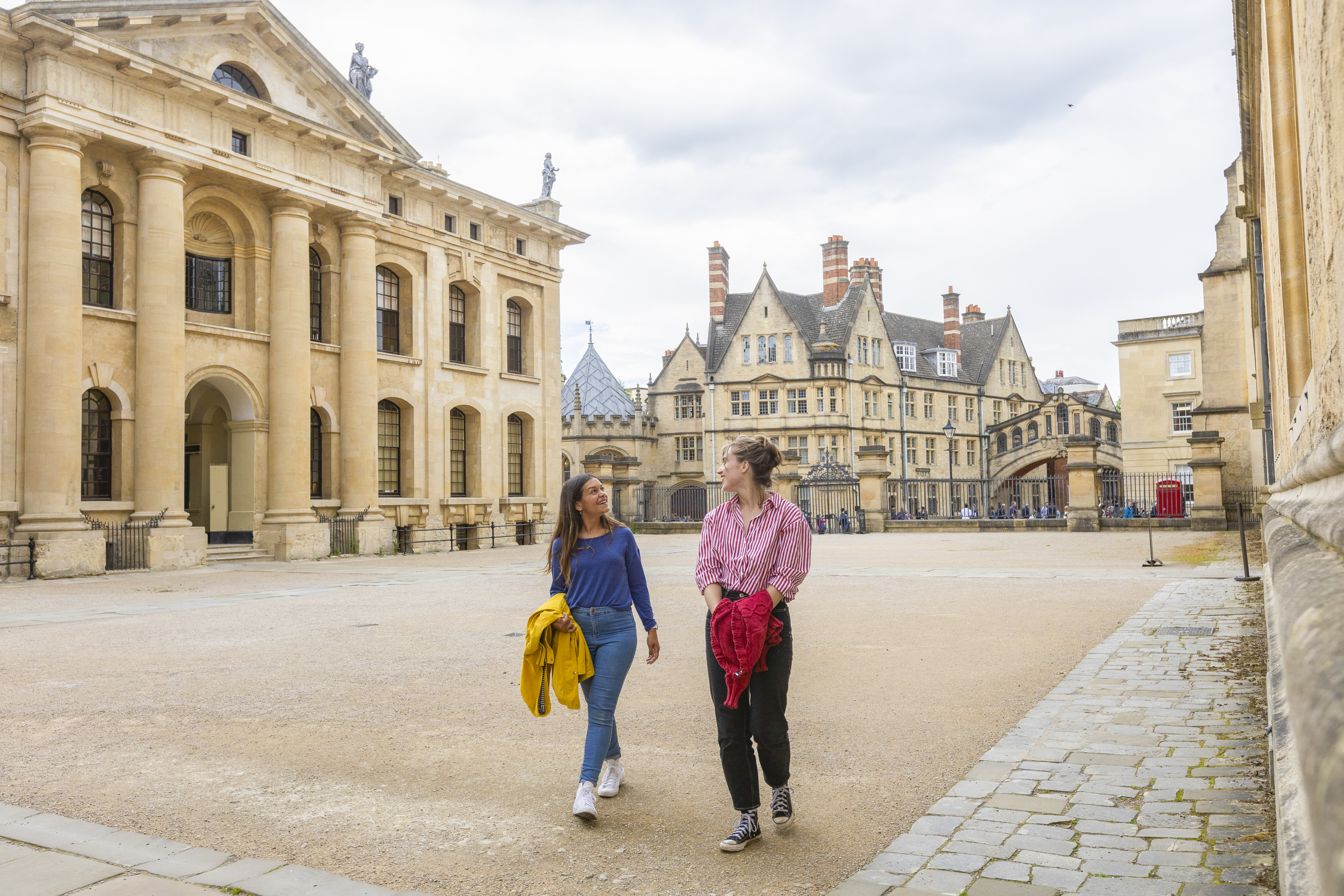 Two women walk across a courtyard among heritage buildings