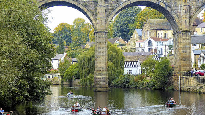 People in rowing boats on a river by a viaduct in a town