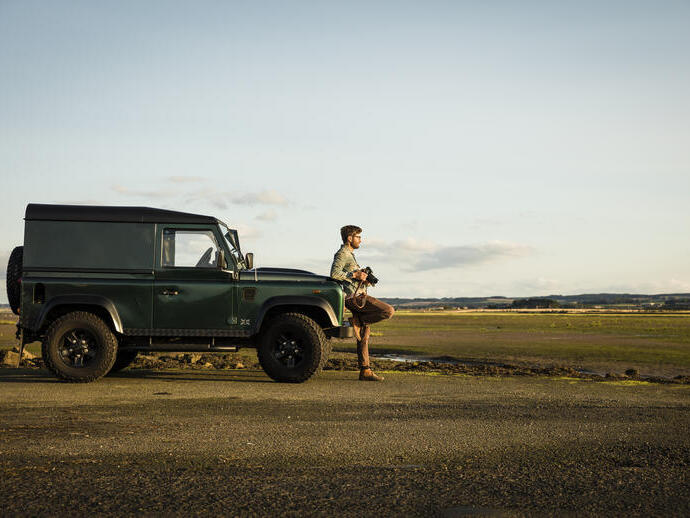 Man leaning against a vehicle, holding camera