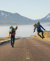 Two men walking and jumping on a road surrounded by mountains