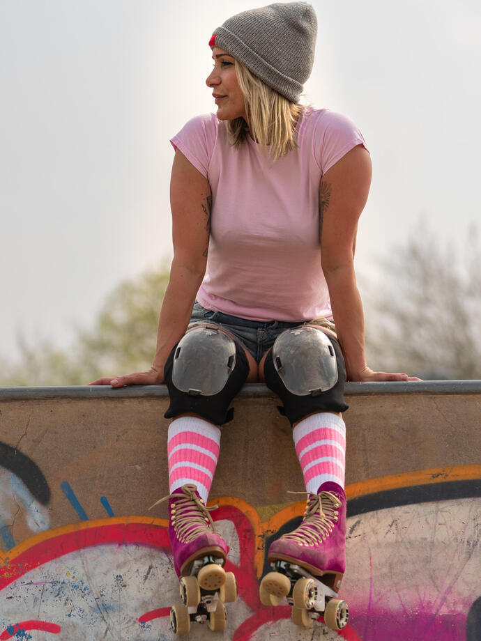 A young woman in rollerskates sitting on the edge of a skate park.