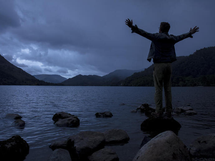 Silhouette of man standing with outstretched arms on shore