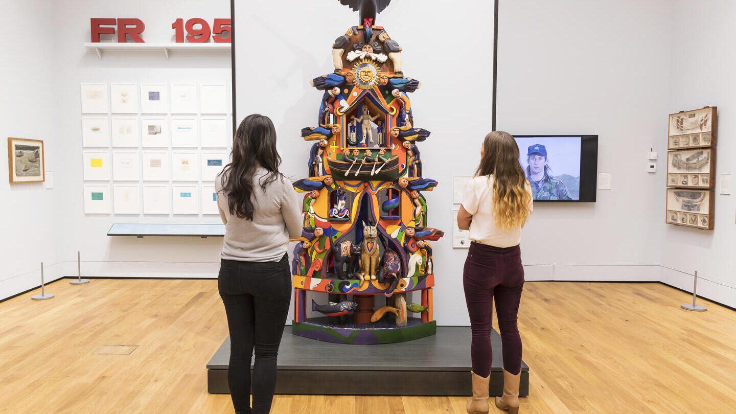 Des gens admirant une sculpture représentant un totem dans une galerie d'art.