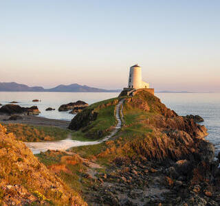 A path leading to a lighthouse on a prominent rocky outcrop by the sea