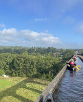 Eine Gruppe paddelt mit Kajaks über einen Viadukt mit malerischem Blick auf den Snowdonia/Eryri-Nationalpark