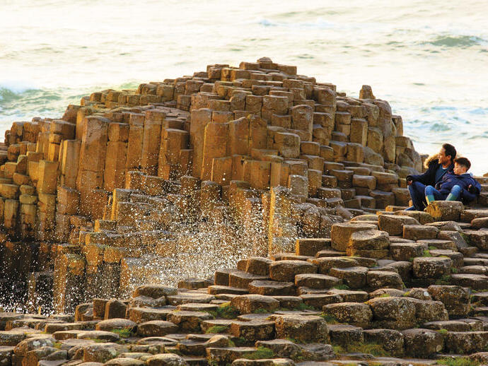 Man and child sitting on rock formations by the sea