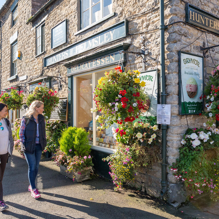 Two women walking past a shop in a village