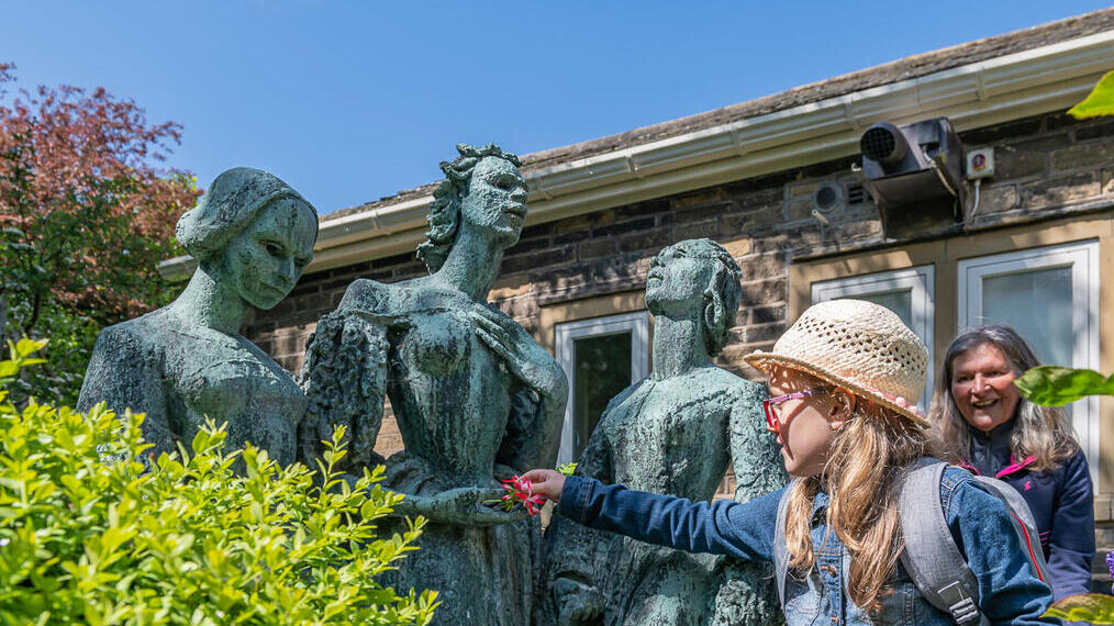 Ein Mädchen legt Blumen in die Hände einer Statue.