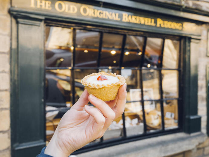 Mano sosteniendo una tarta Bakewell delante de una panadería