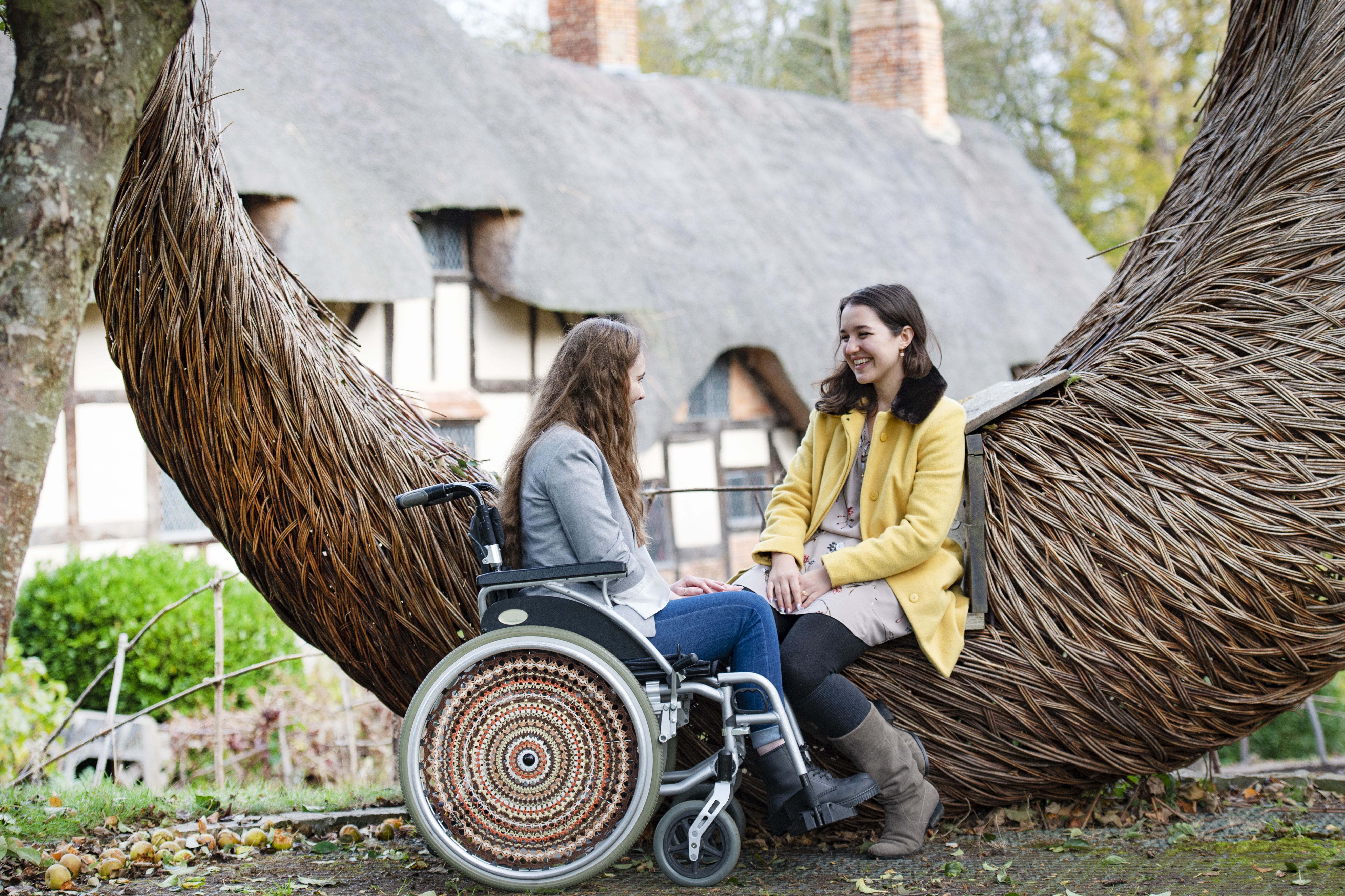 Wheelchair user and friend sat beside a wooden sculpture