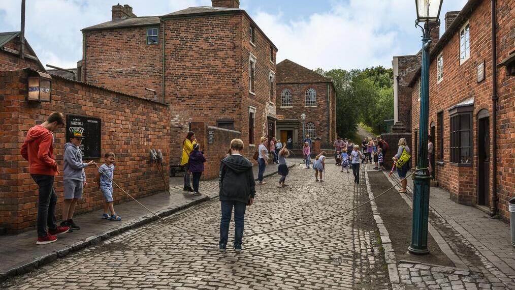 People standing in a street at a living museum, playing old fashioned games