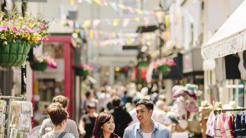 Couple holding hands, walking through a busy pedestrian street with stalls and shops either side