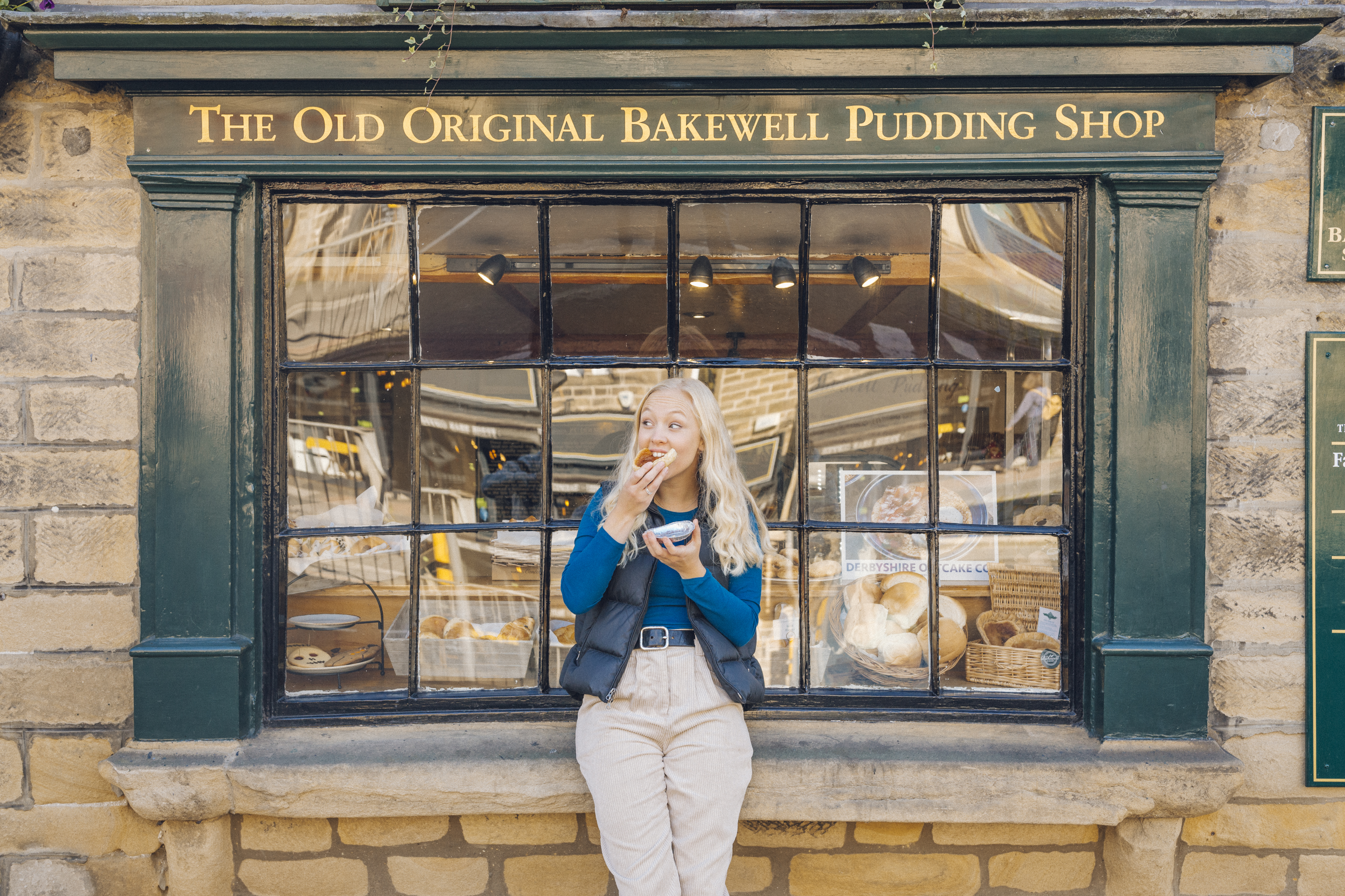 Woman eating bakewell tart in front of bakery