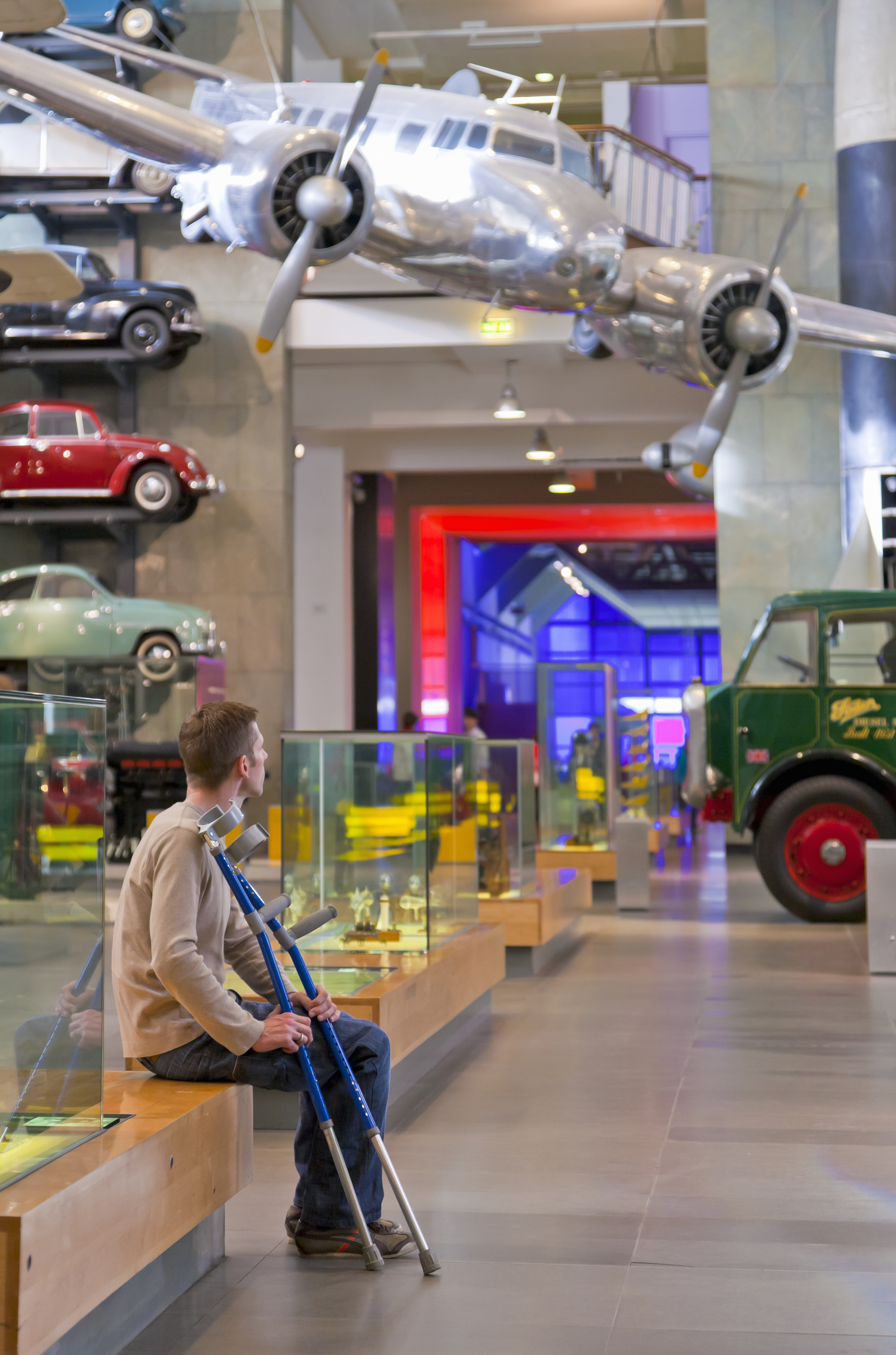 Man sitting down, looking at the displays in a museum holding his crutches