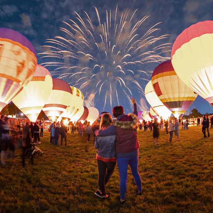 Couple watching grounded hot air balloons and fireworks in the night sky