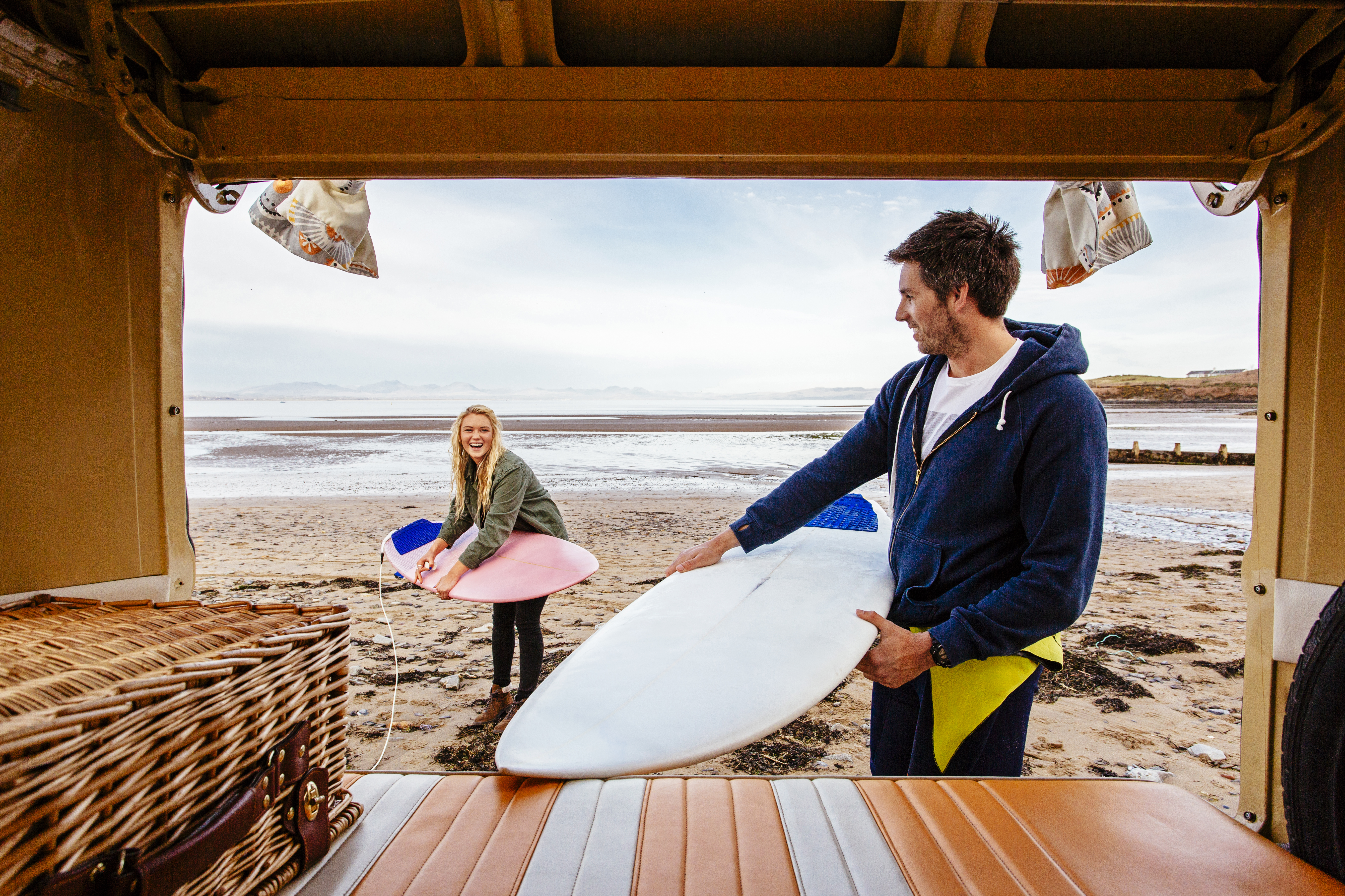 Un homme et une femme déchargent des planches de surf d'un camping-car sur la plage