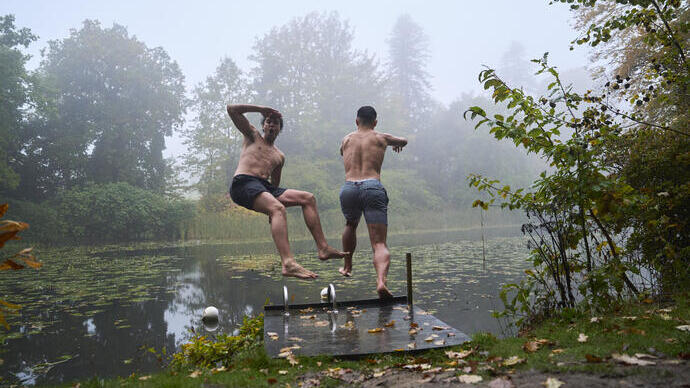 Two men jump off the swimming platform into a lake in an autumnal setting
