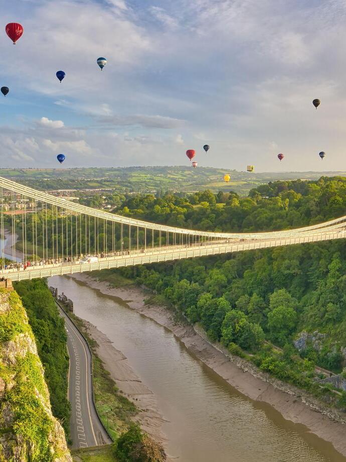 Aerial view of a large suspension bridge with hot air balloons taking to the air