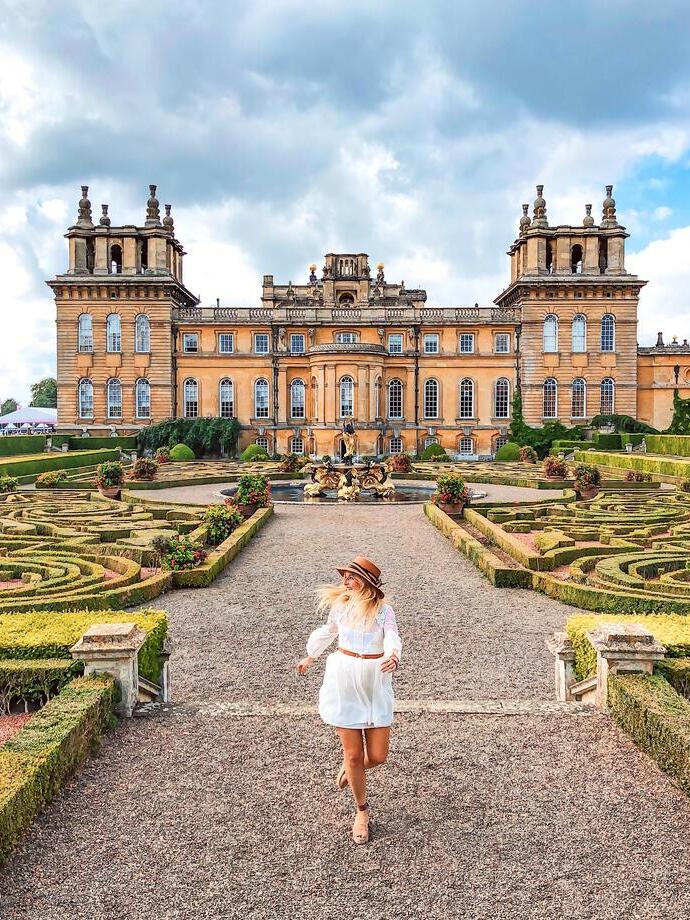 Woman walking in Blenheim Palace gardens surrounded by greenery and manicured topiary.