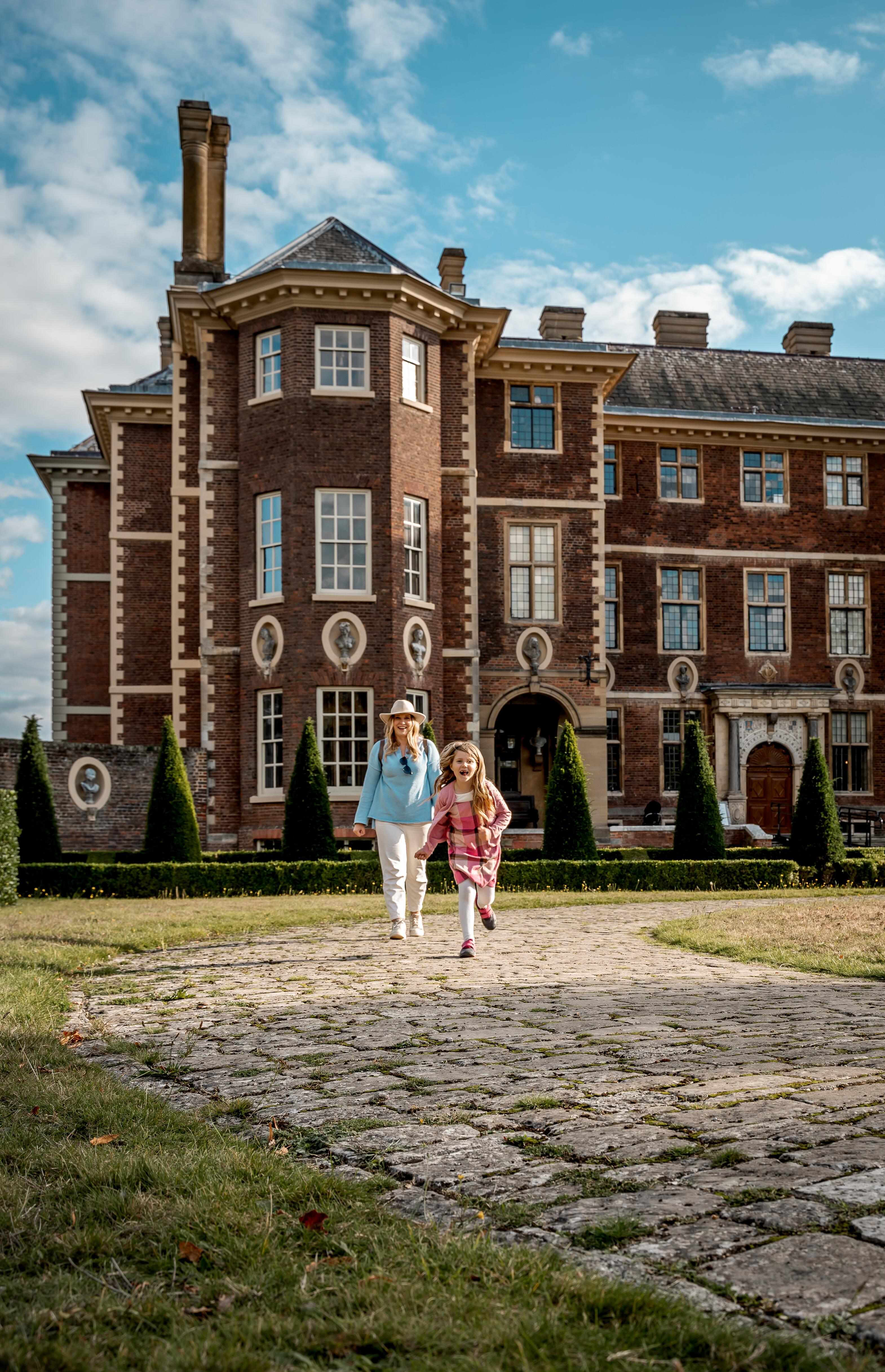 A mother walks and a daughter runs in front of Ham House.