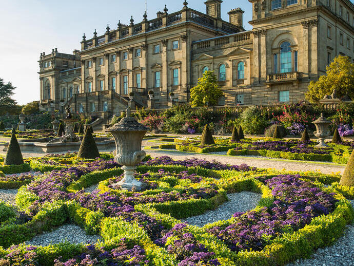 A formal garden with statues and low hedges in front of a stately house