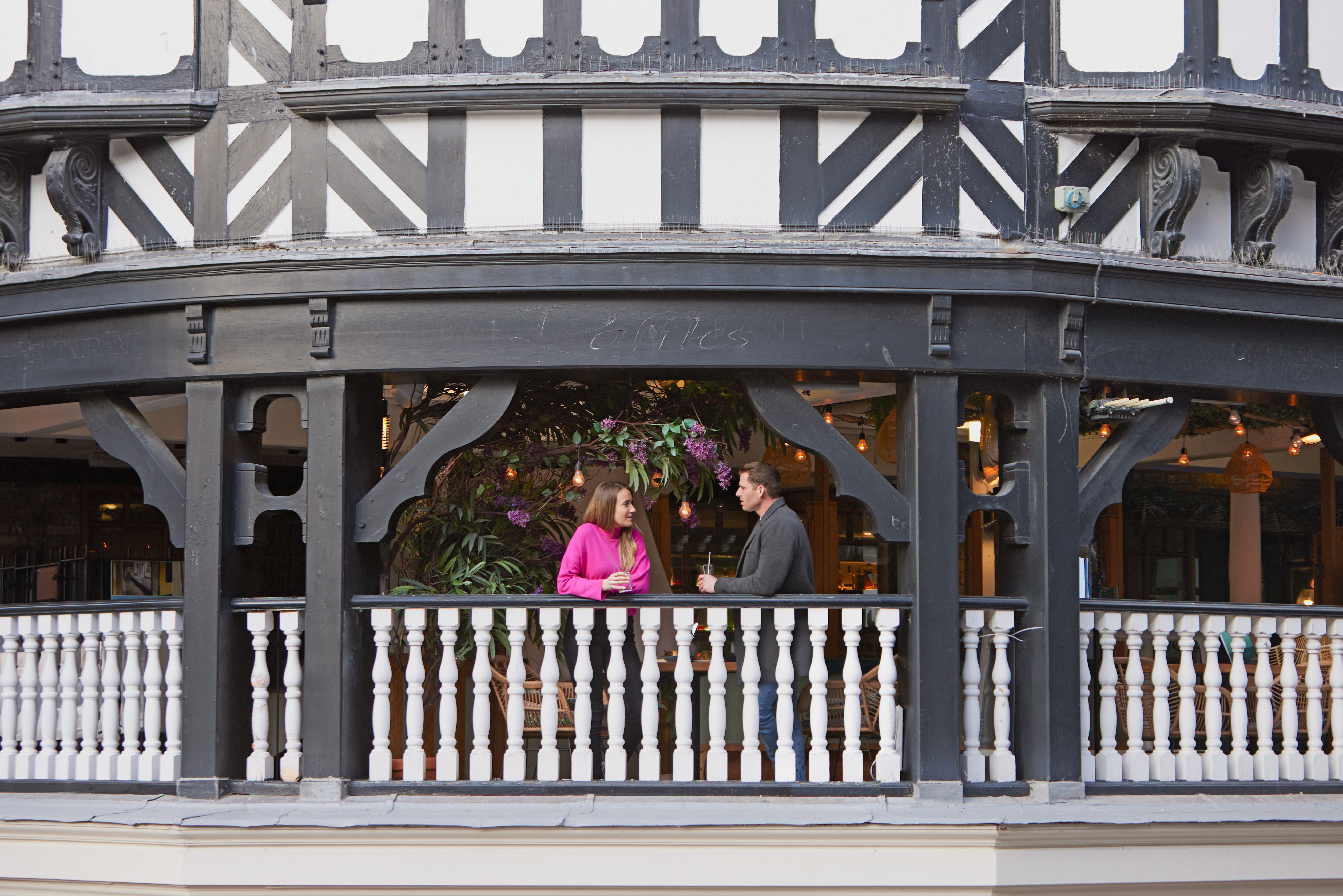 A man and a woman have a drink and talk on the balcony at a local cafe.