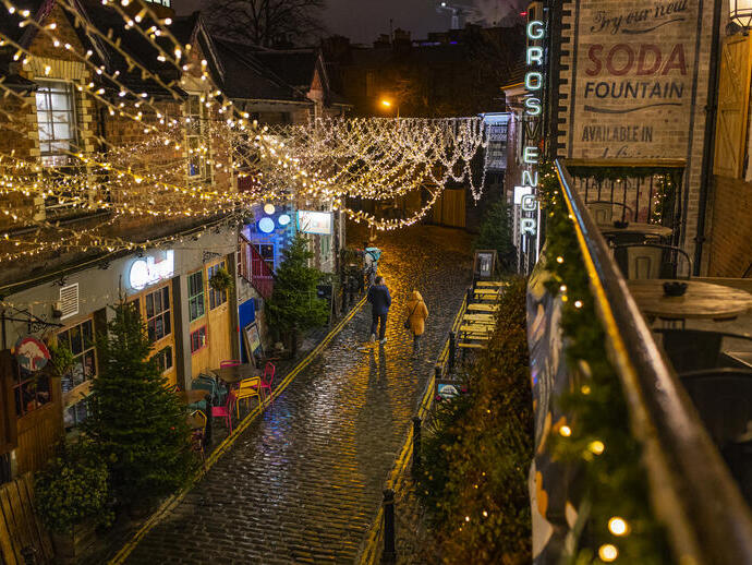 Couple marchant le long d'une rue pavée la nuit, décorée de guirlandes lumineuses