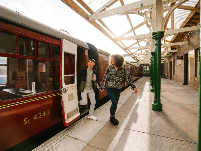 A man and a woman stepping out of an old style train carriage.