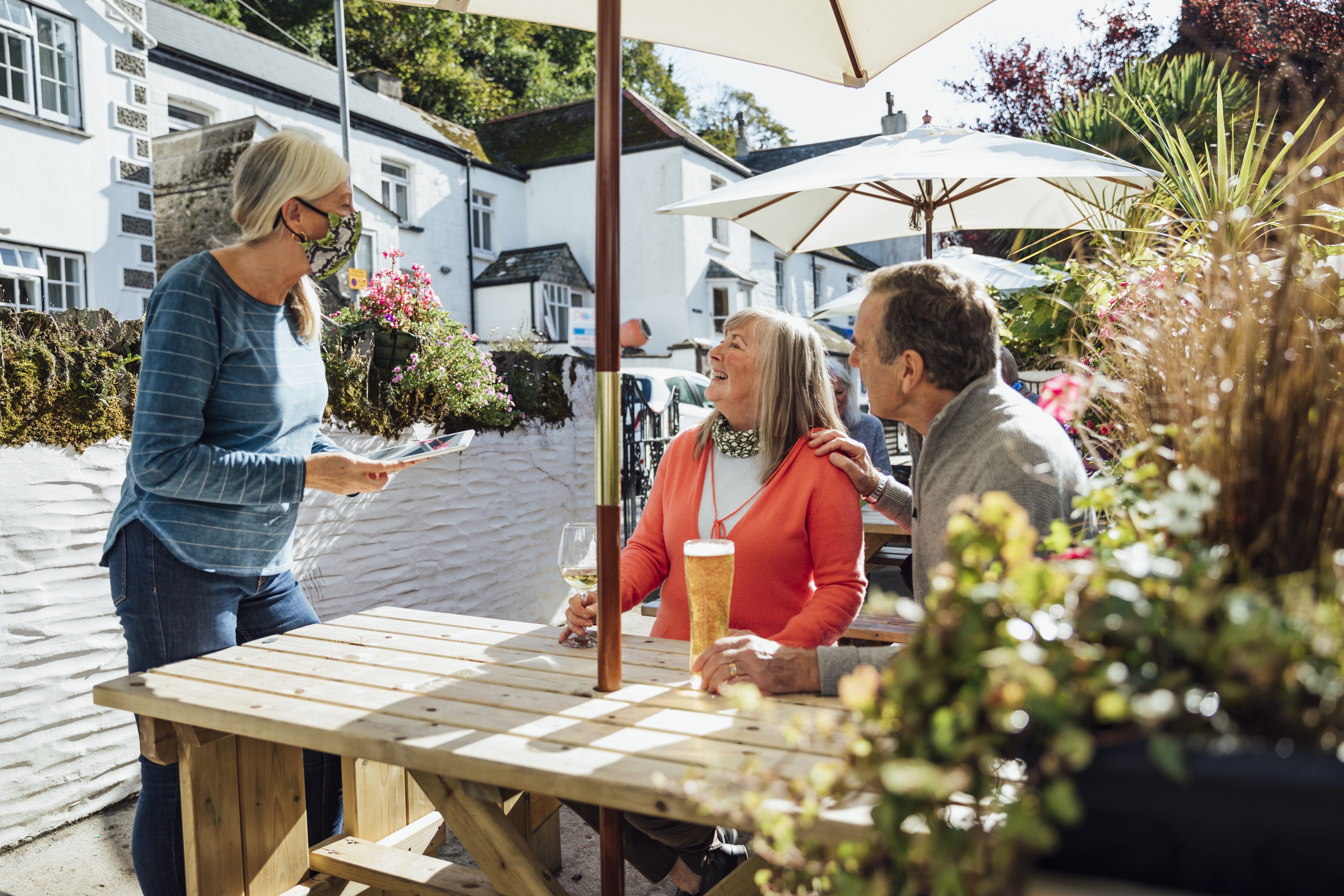 Couple sitting outside at a pub having a drink, talking to a member of staff