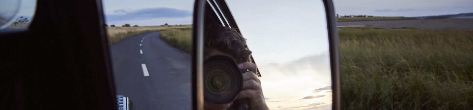Reflection of a man with a camera in the side mirror of a car